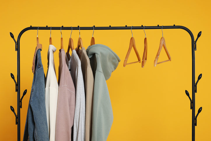 A few items of clothing hanging on a clothes rack against a yellow backdrop