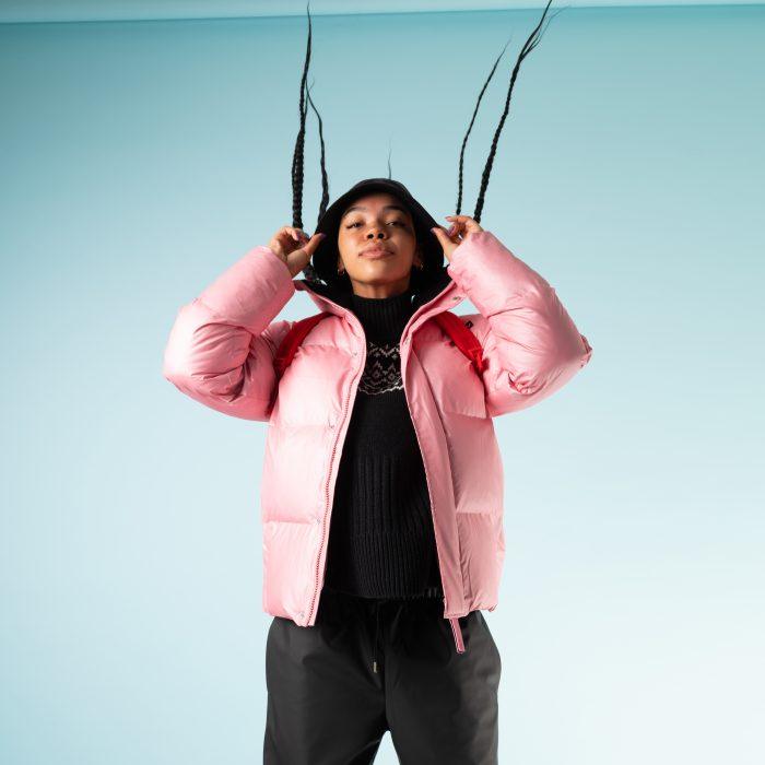 A young woman wear a pink Rains puffer against black cloting
