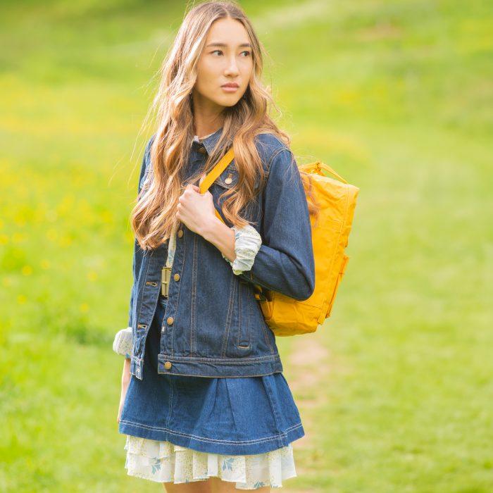 Woman wears festival attire and carries a mustard Fjallraven backpack