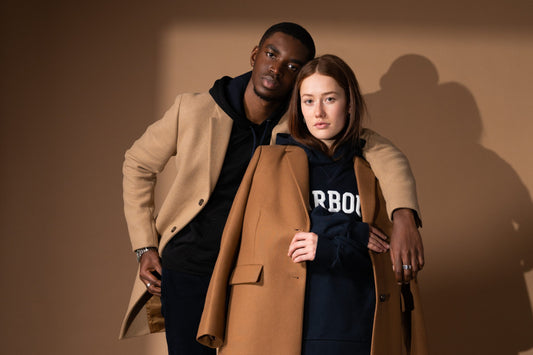 Young man and woman wear beige overcoats over black sweatshirts