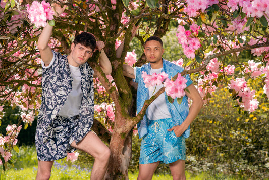 Two men pose under a cherry tree in stylish matching shirts and short sets