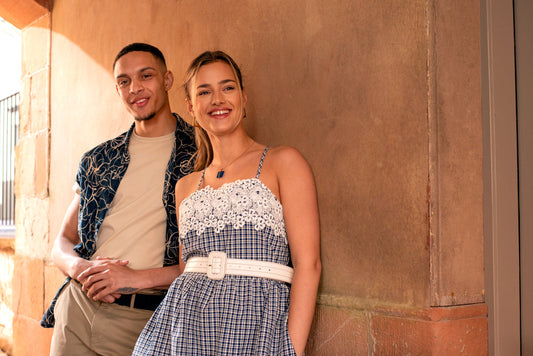 A man and woman stand under an archway in the summer attire posing in shade from the sun