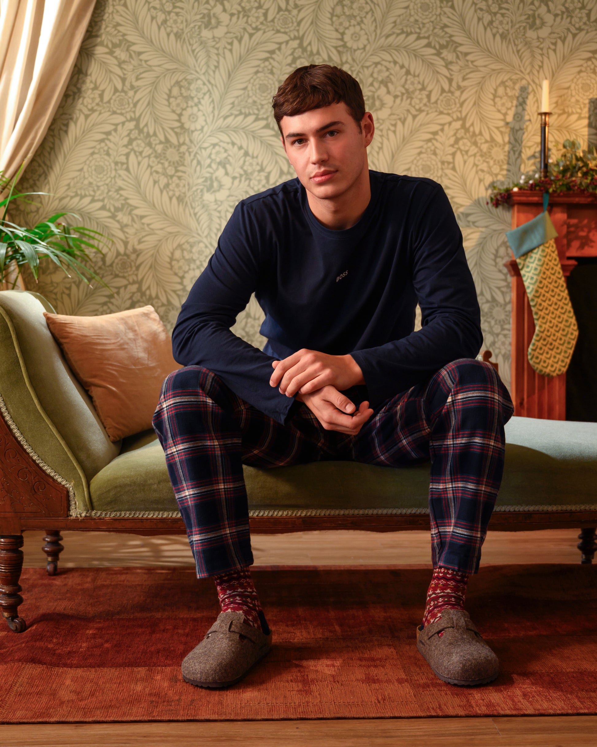 Man sitting on a couch wearing navy pajama top and plaid pants in a cozy living room.