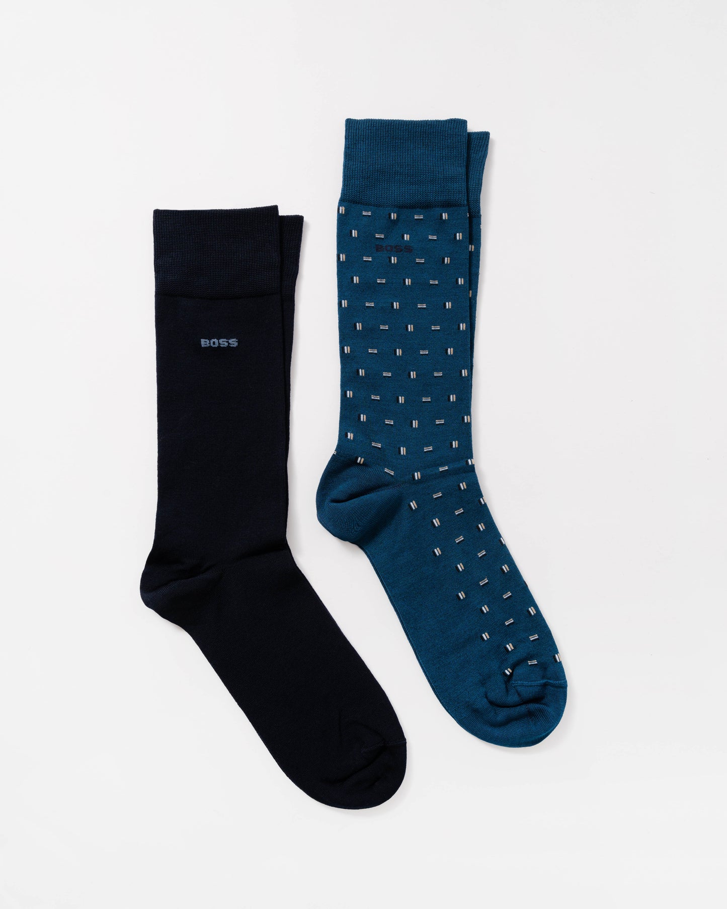 Two pairs of BOSS crew socks on a light gray background: one pair is solid black with a small BOSS logo, and the other pair is dark teal with a small white geometric pattern.
