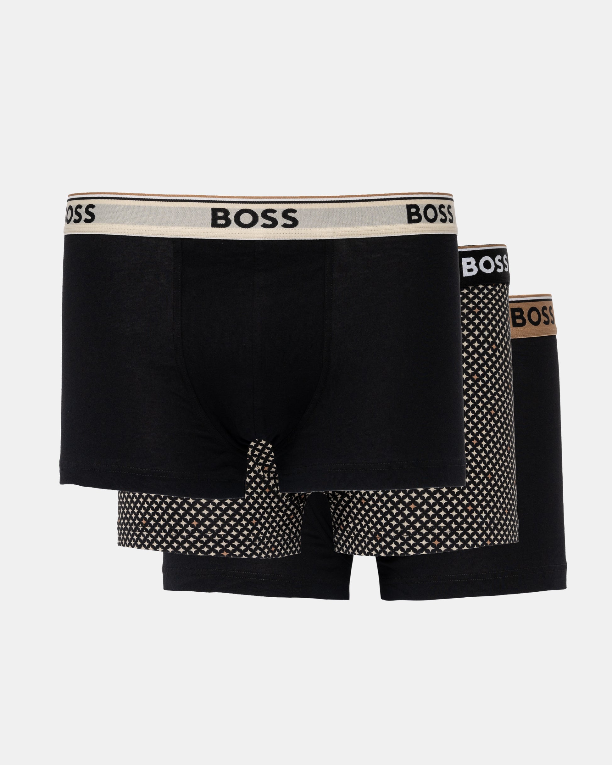 Three BOSS men's boxer briefs in black, arranged in a 3-pack. The front pair has a beige waistband with black BOSS lettering, while the pairs behind it feature black and white polka-dot patterns on the legs and a brown BOSS logo on their waistbands.