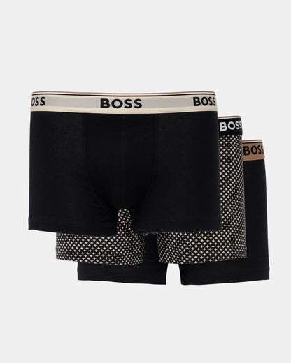Three BOSS men's boxer briefs in black, arranged in a 3-pack. The front pair has a beige waistband with black BOSS lettering, while the pairs behind it feature black and white polka-dot patterns on the legs and a brown BOSS logo on their waistbands.