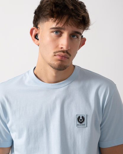 Man wearing a light blue t-shirt with a logo on a plain background