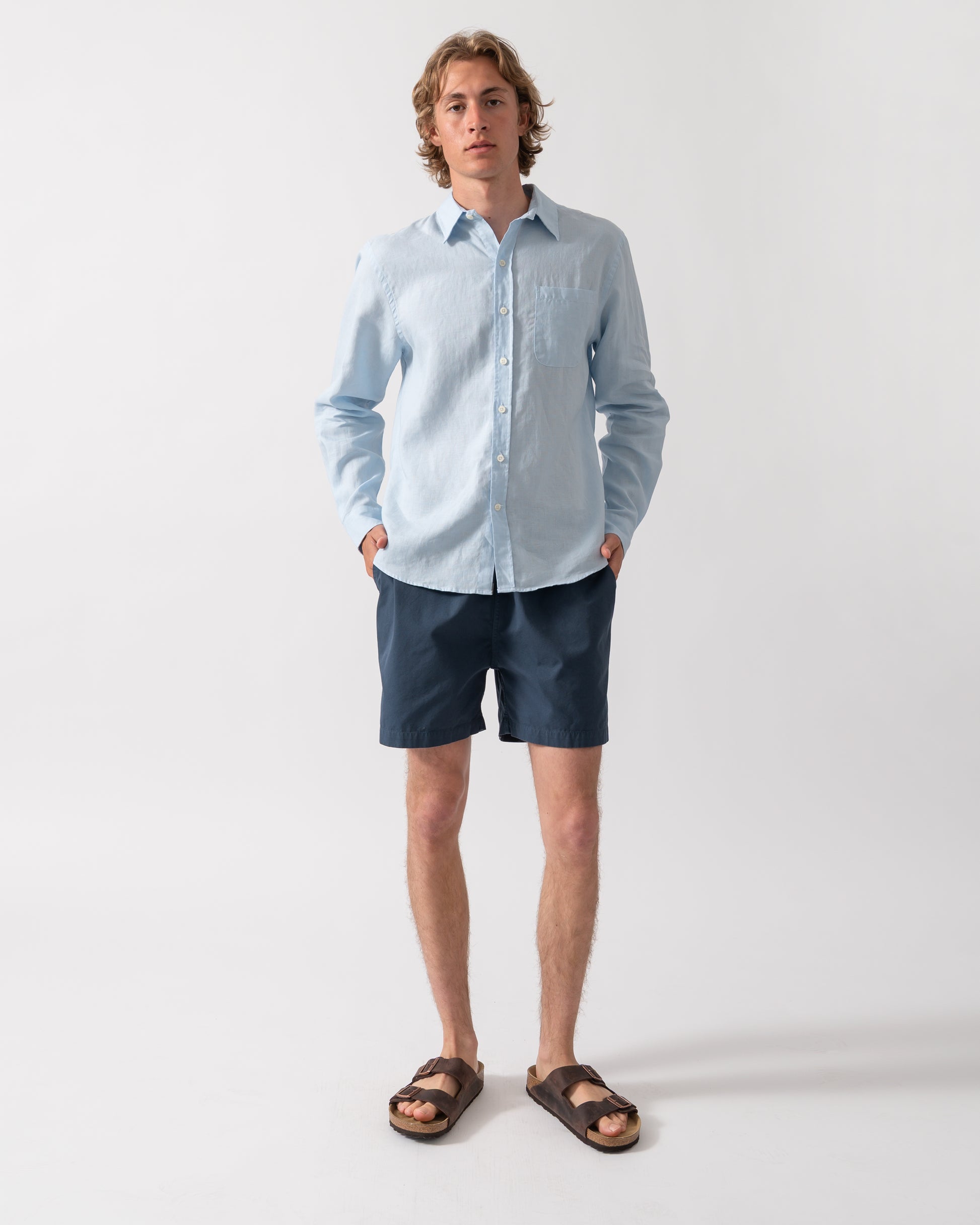 full length shot of a Model wearing a Colorful Standard Mens Long Sleeve Linen Shirt in Polar Blue
