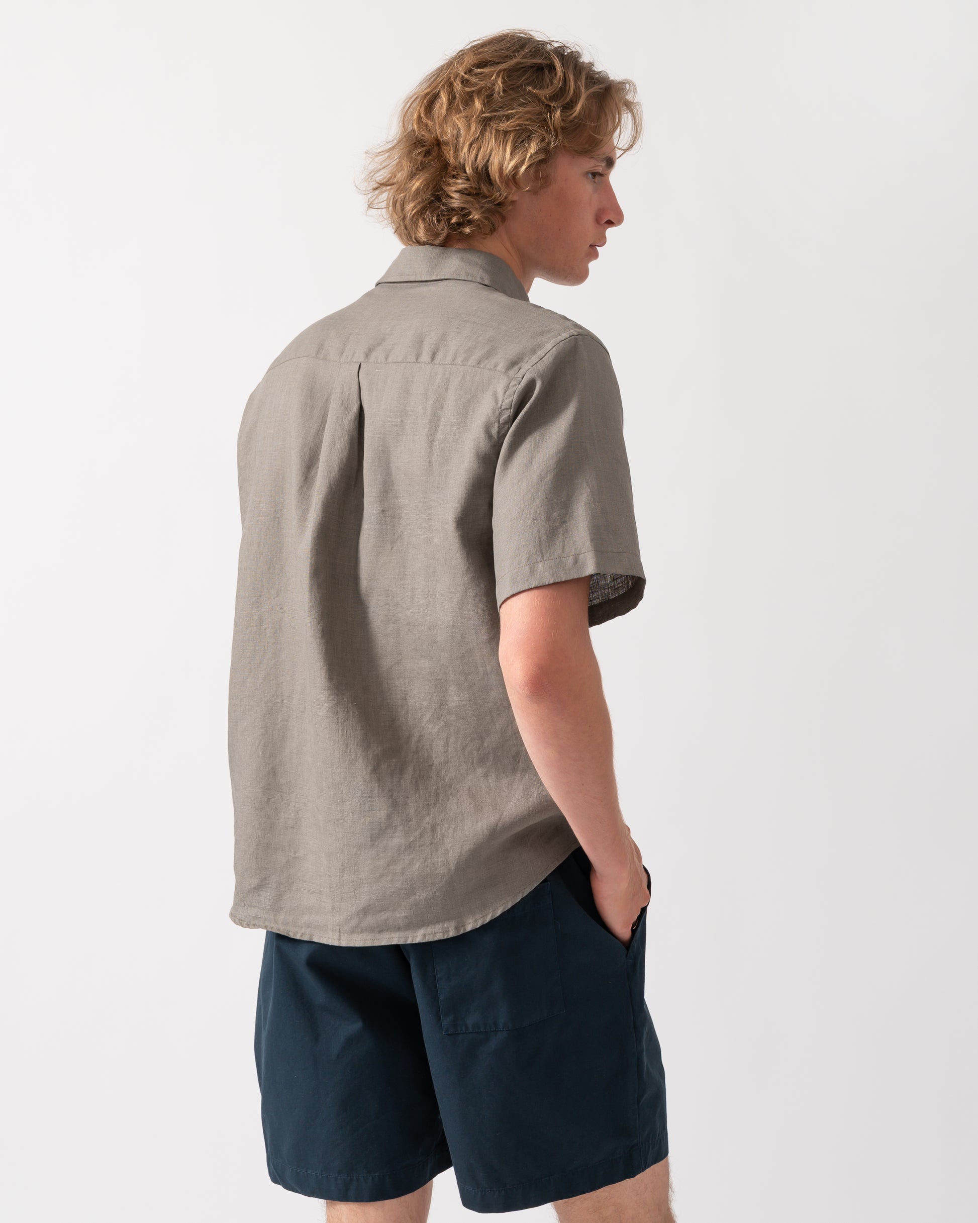 back shot of a model wearnig a Colorful Standard Mens Short Sleeve Linen Shirt in Dusty Olive