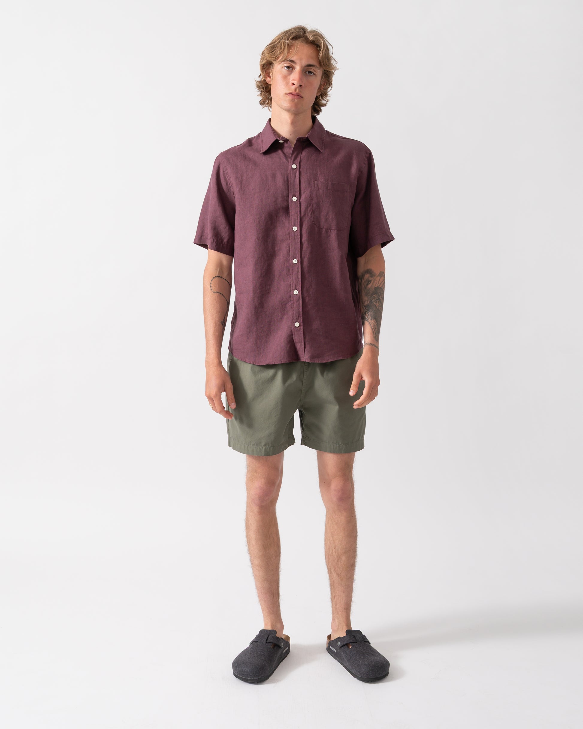 full length shot of a model wearing a Colorful Standard Mens Short Sleeve Linen Shirt in Oxblood Red