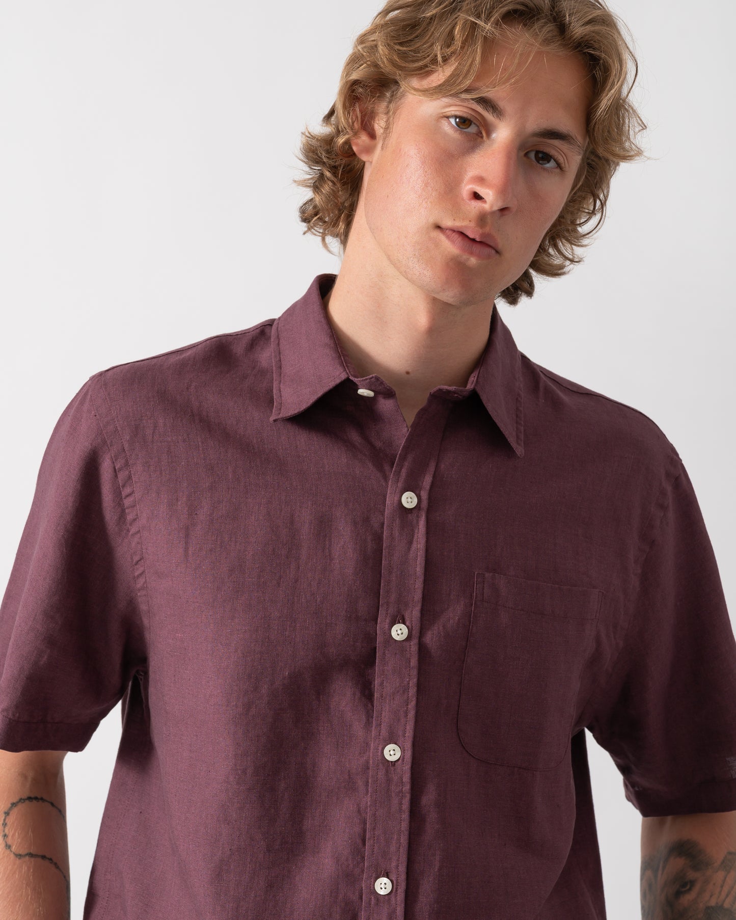 close up shot of a model wearing a Colorful Standard Mens Short Sleeve Linen Shirt in Oxblood Red