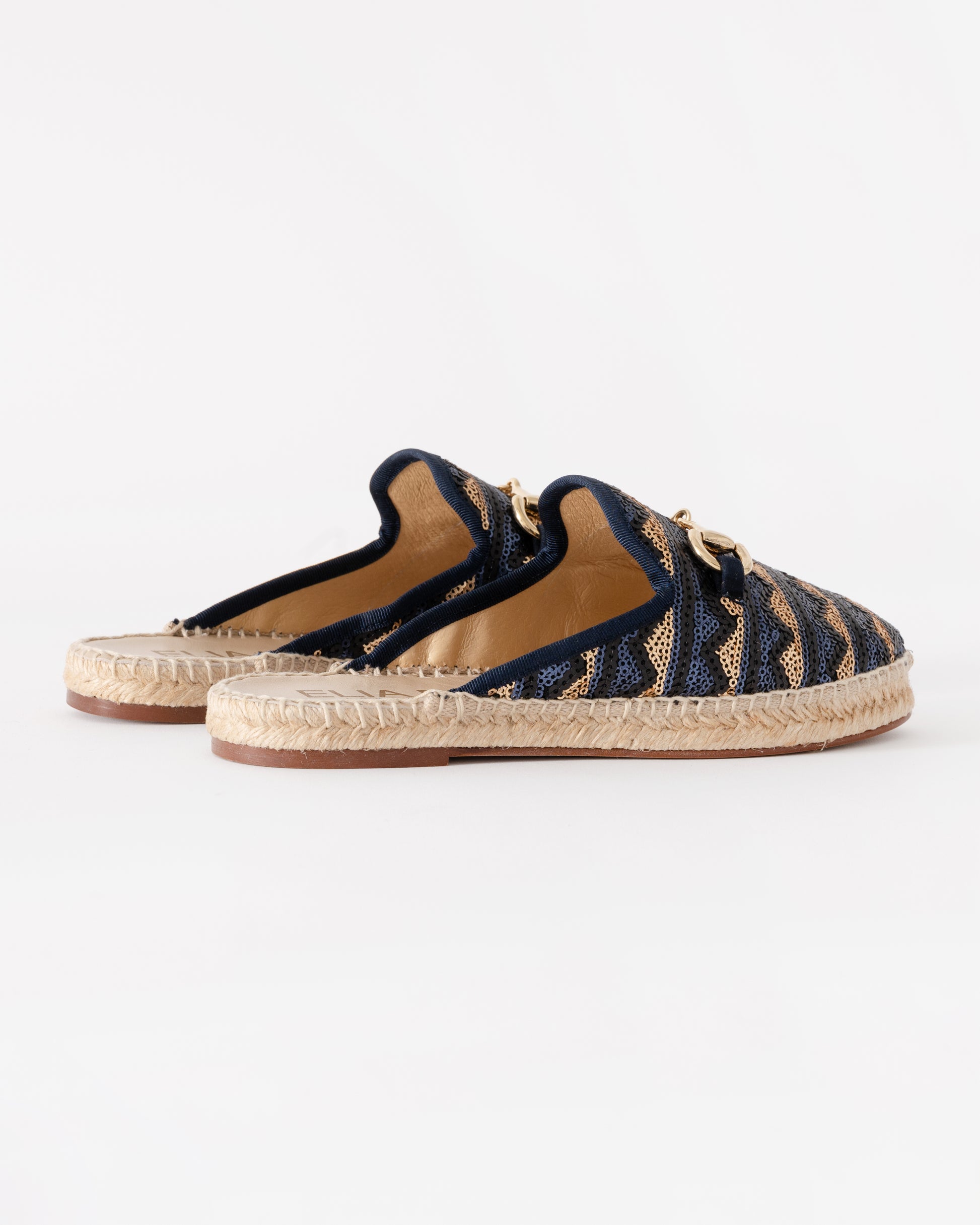 Pair of navy blue espadrilles with gold accents on a white background