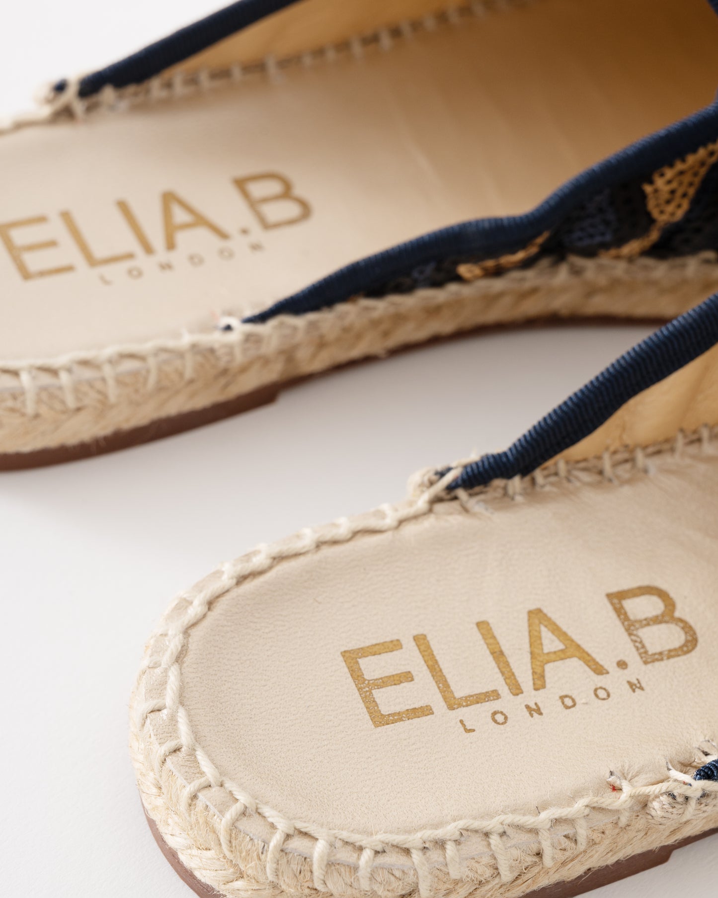 Close-up of Elia B London sandals with braided details on a white background