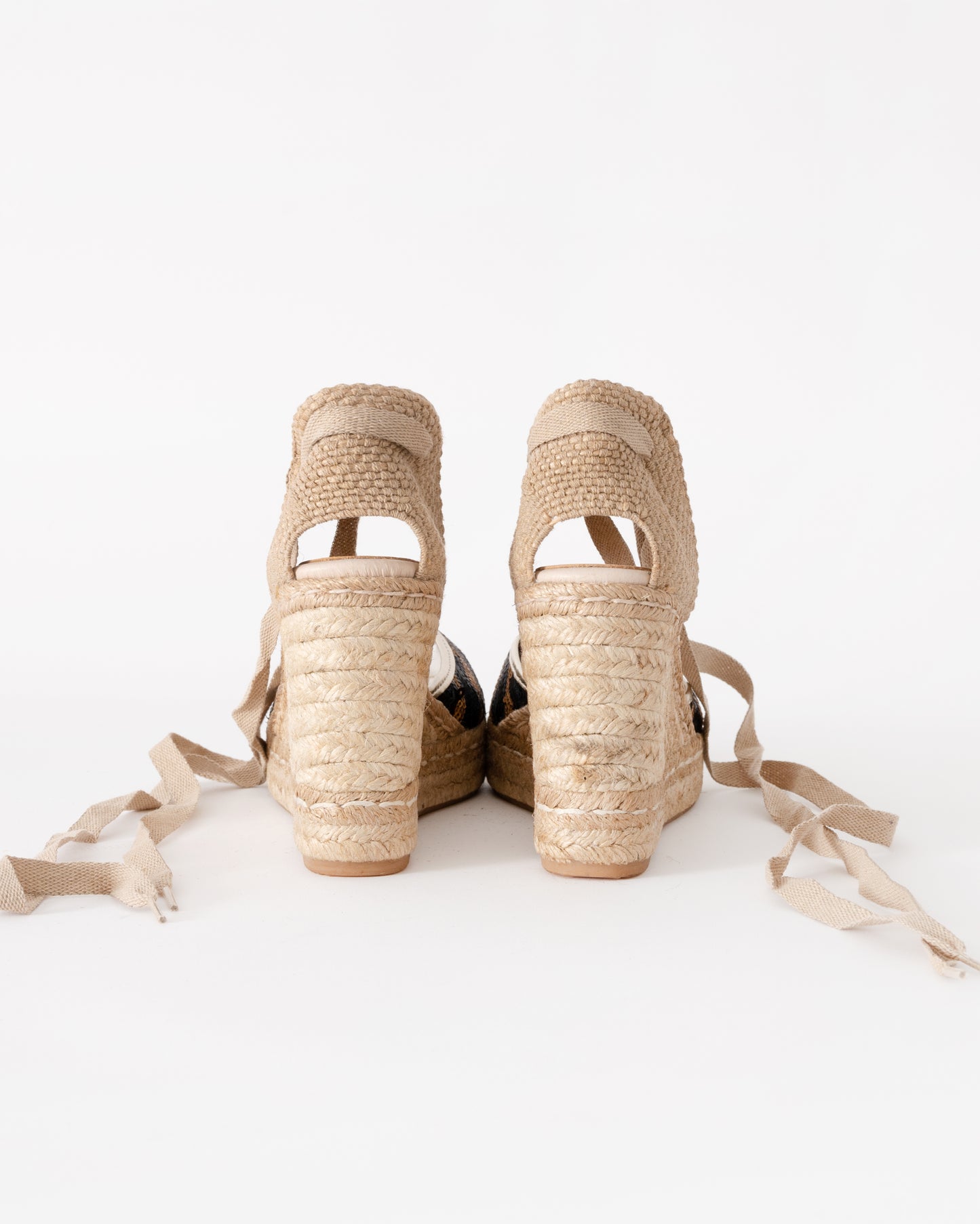 Pair of beige wedge sandals with raffia straps on a white background