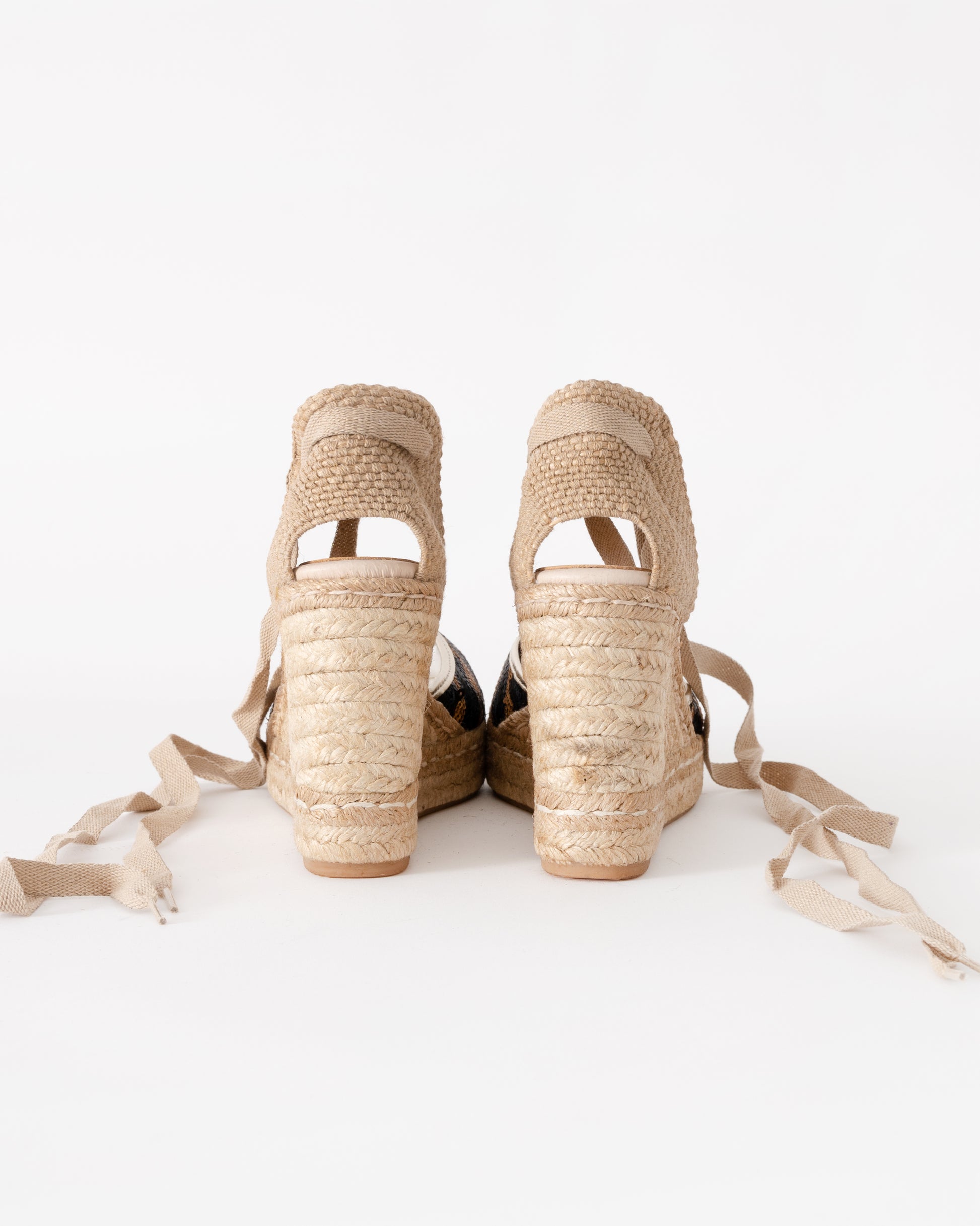 Pair of beige wedge sandals with raffia straps on a white background