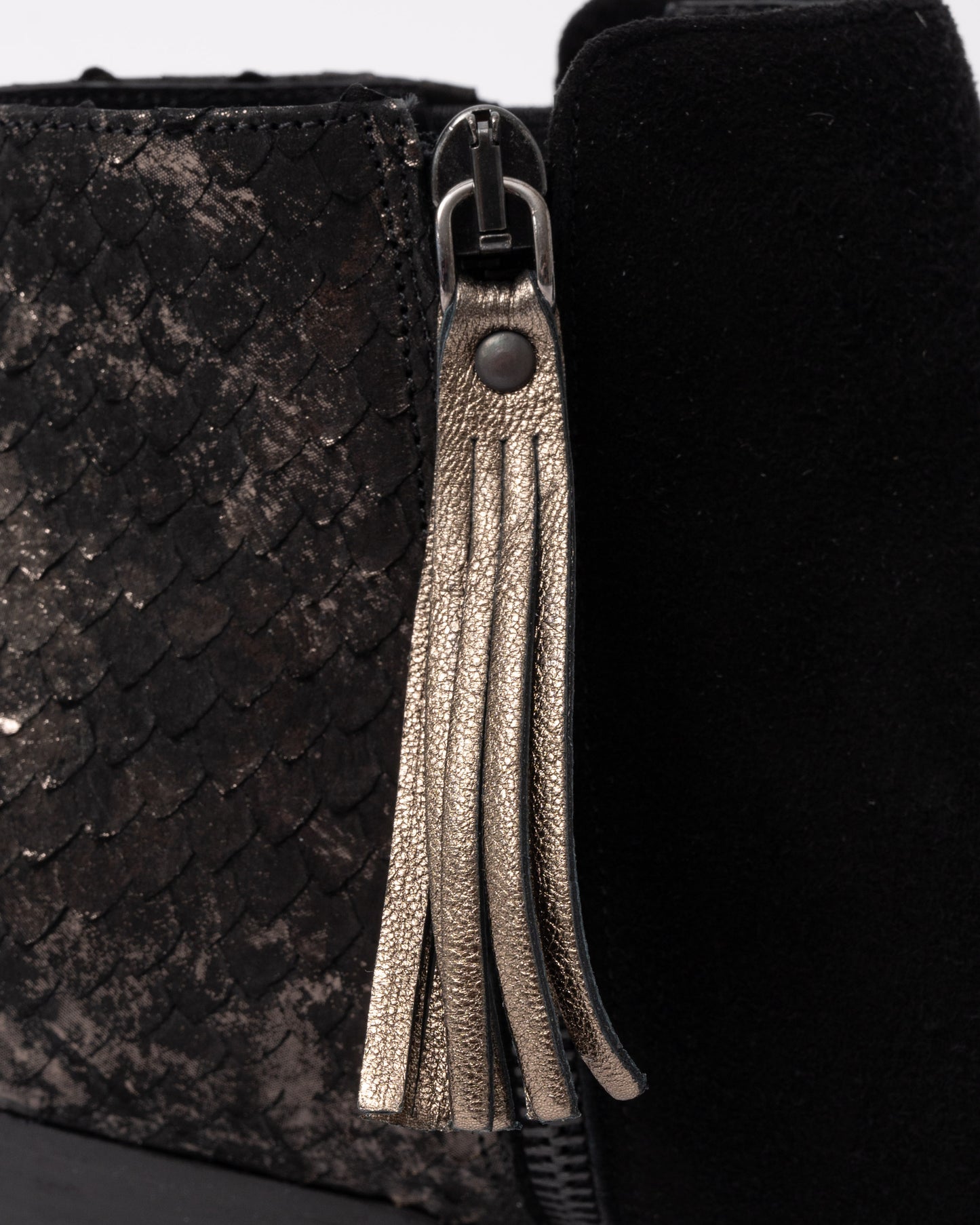 Close-up of a black textured bag with a silver zipper and tassel.