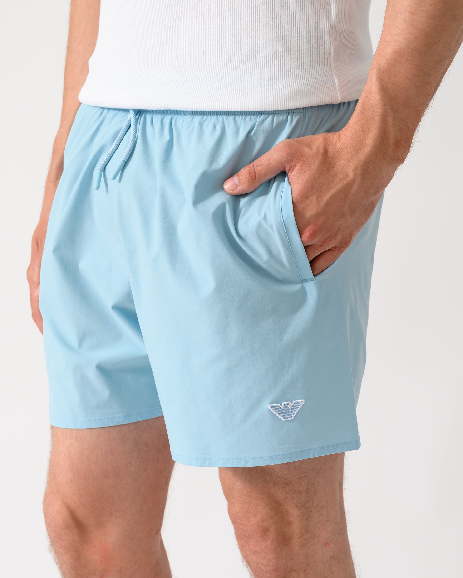 side shot of a model wearing a pair of Emporio Armani Mens Swim Shorts with Eagle Logo in Sky