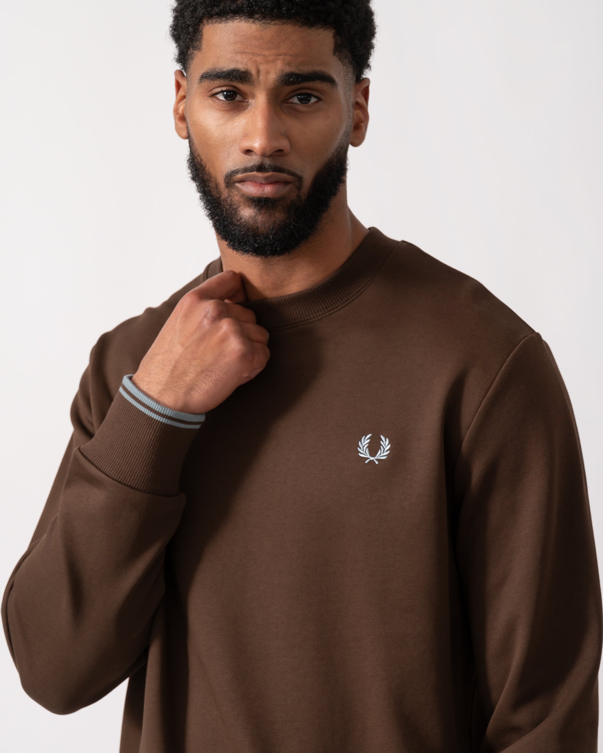 close up of a Model wearing a Fred Perry Mens Crew Neck Sweatshirt in Burnt Tobacco with Stockport Blue trim and logo