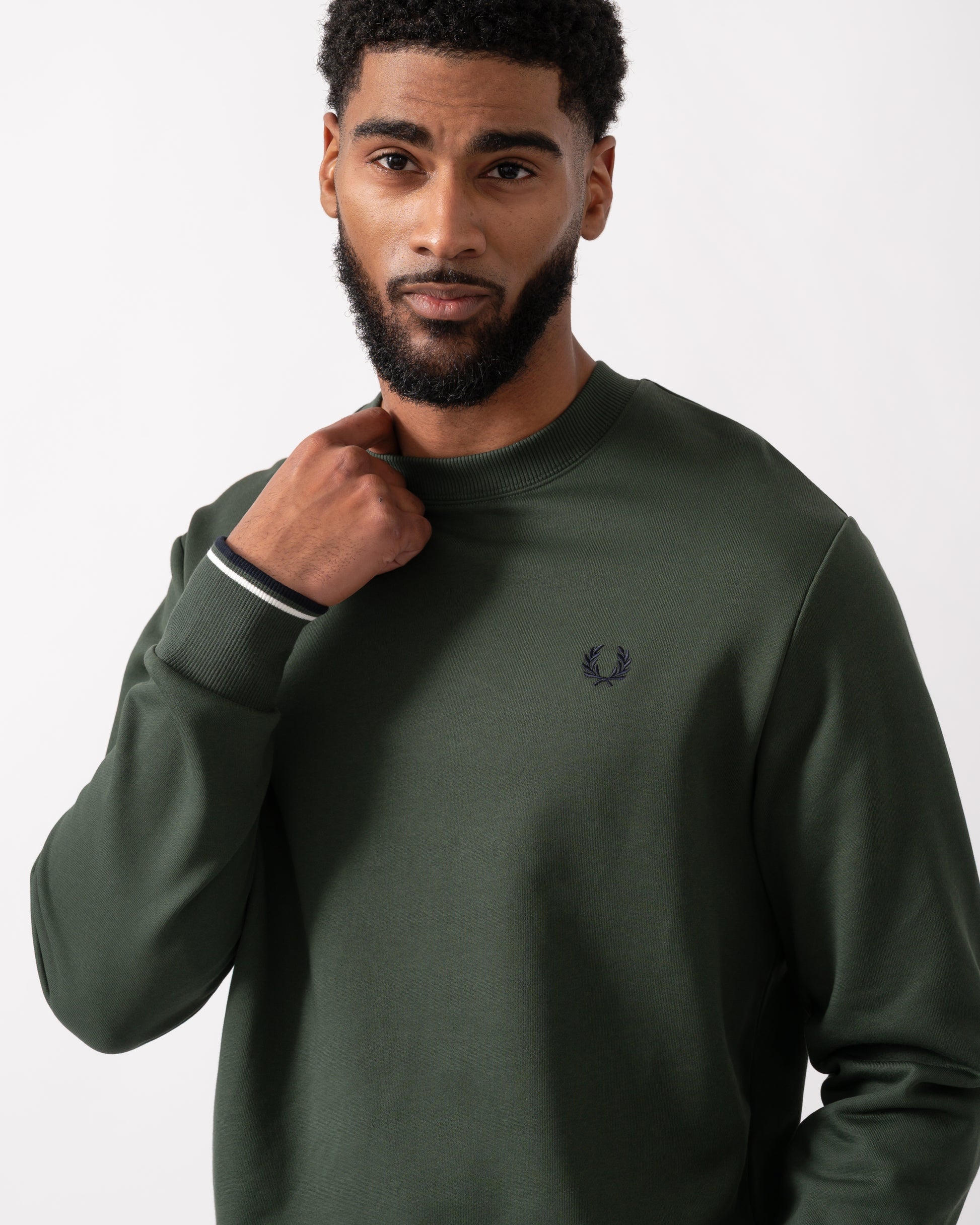 close up of a model wearing a Fred Perry Mens Crew Neck Sweatshirt in Court Green, with Snow White trim and Navy logo
