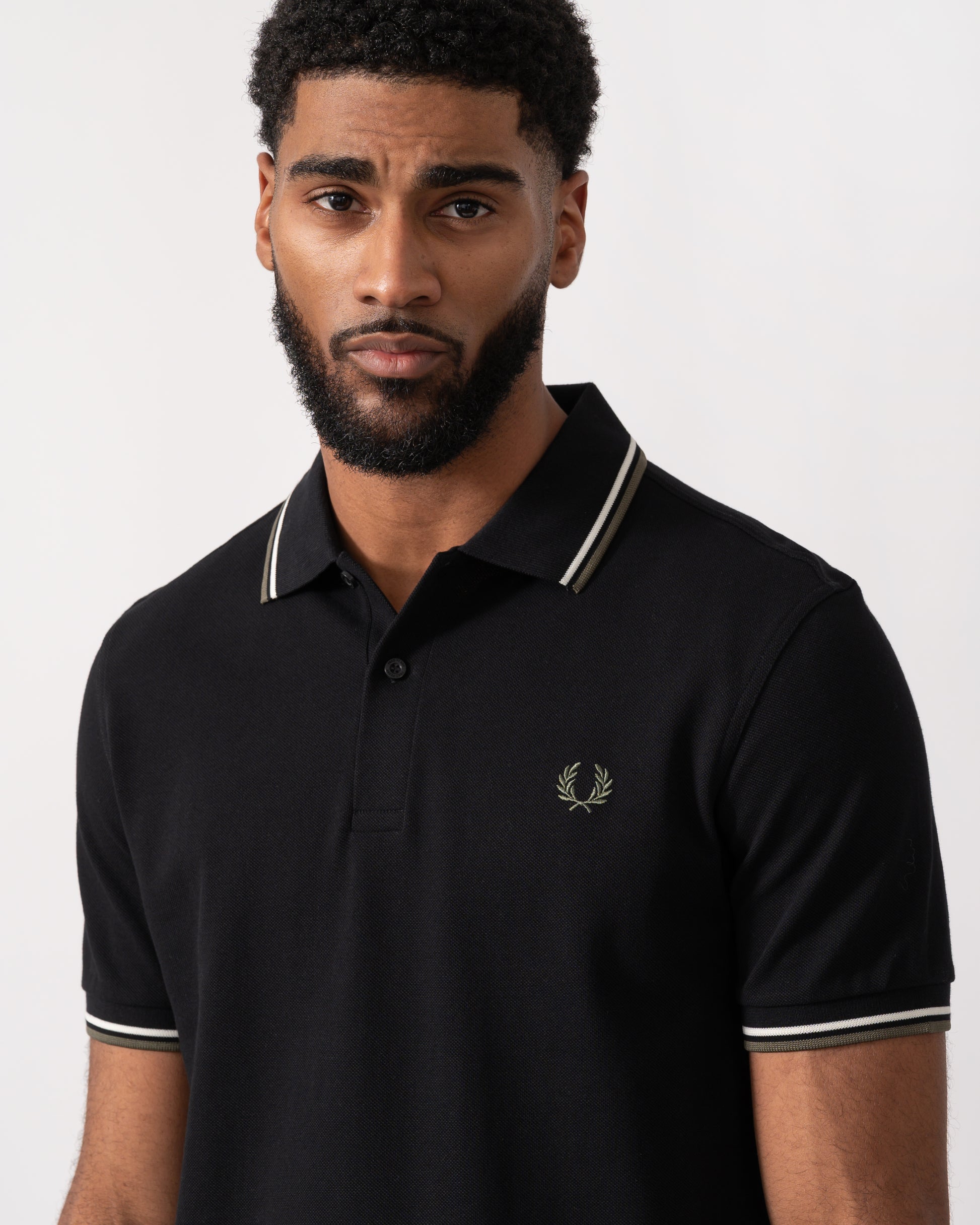 close up of a model wearing a Fred Perry Mens Twin Tipped Signature Polo Shirt in Black with Ecru and Laurel Wreath Green trim