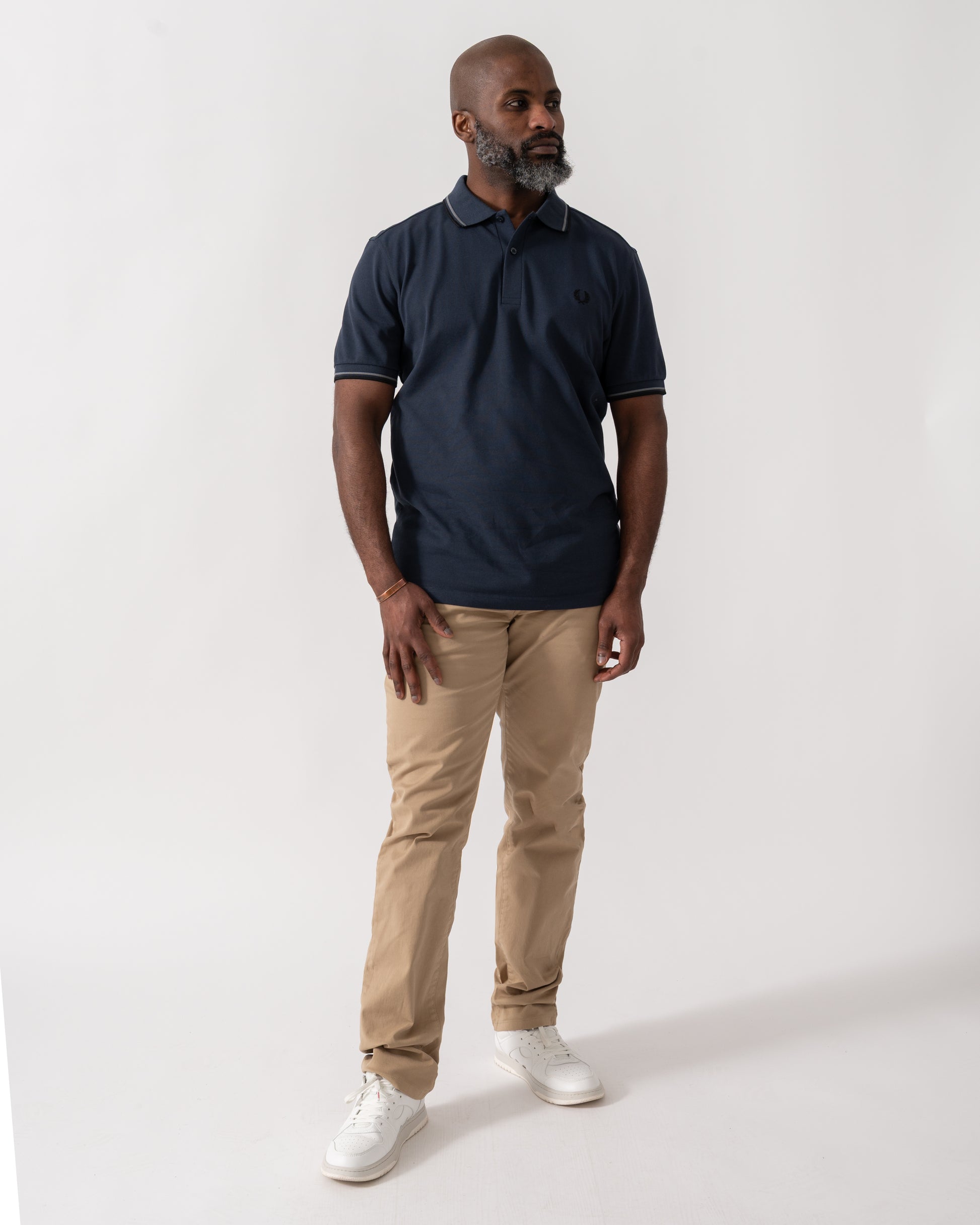 full length shot of a model wearing a Fred Perry Mens Twin Tipped Signature Polo Shirt in Dark Airforce with Stockport Blue and Black trim