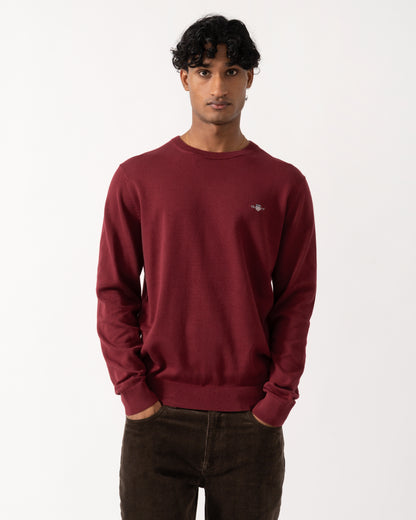 Studio photograph of a model wearing a GANT Mens Classic Cotton Shield Logo Crew Neck Jumper in 676 Deep Grape Wine