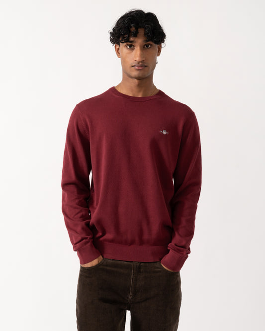 Studio photograph of a model wearing a GANT Mens Classic Cotton Shield Logo Crew Neck Jumper in 676 Deep Grape Wine
