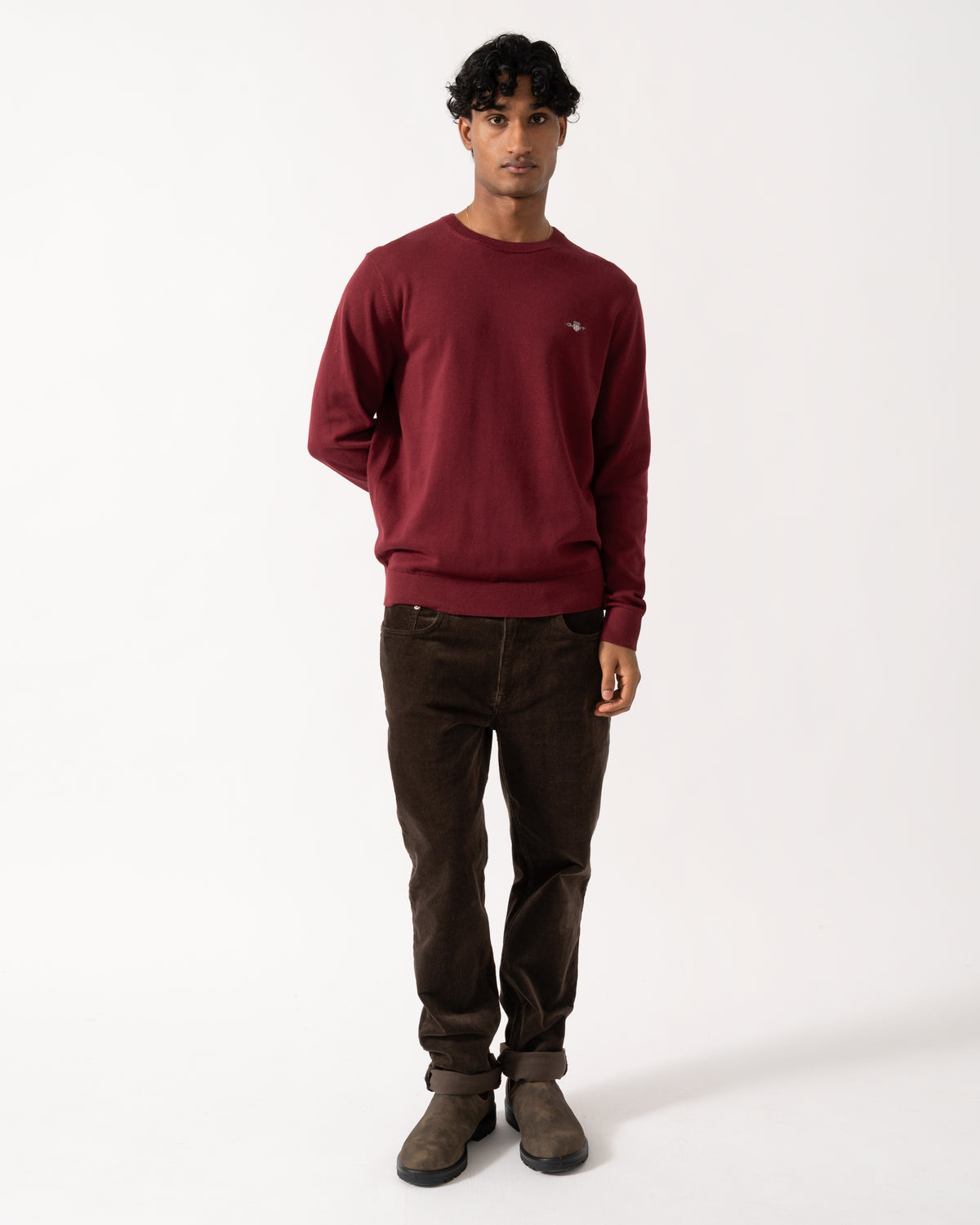 full length Studio photograph of a model wearing a GANT Mens Classic Cotton Shield Logo Crew Neck Jumper in 676 Deep Grape Wine