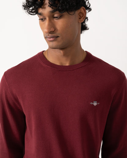 close up Studio photograph of a model wearing a GANT Mens Classic Cotton Shield Logo Crew Neck Jumper in 676 Deep Grape Wine