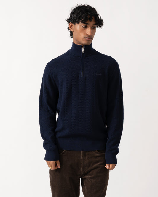 Studio photograph of a model wearing a GANT Mens Herringbone Texture Half Zip Sweater in 433 Evening Blue