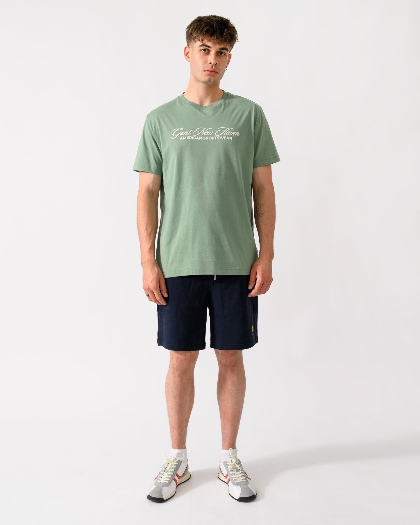 full length shot of a model wearing a GANT Mens Logo Graphic Short Sleeve T-Shirt in 308 Surplus Mint