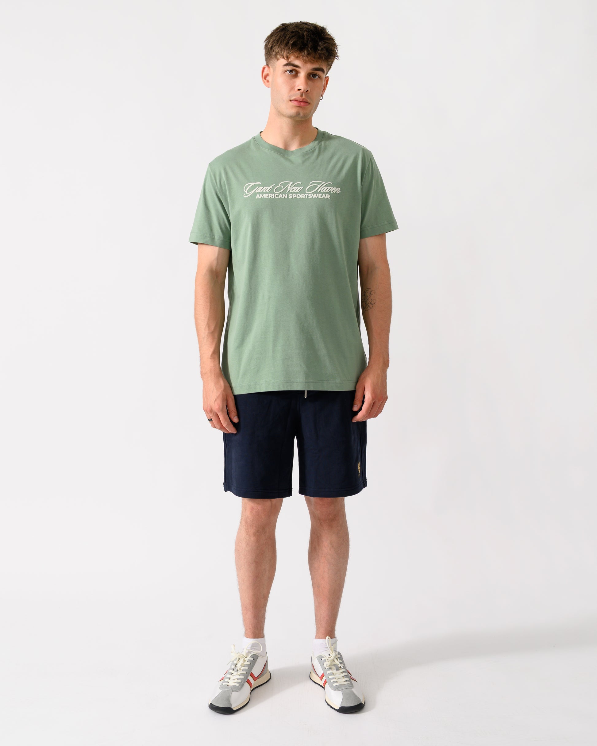 full length shot of a model wearing a GANT Mens Logo Graphic Short Sleeve T-Shirt in 308 Surplus Mint
