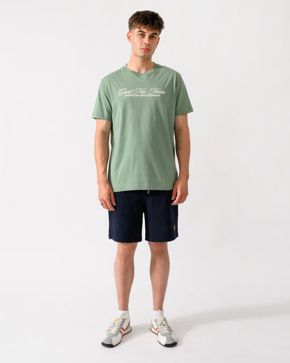 full length shot of a model wearing a GANT Mens Logo Graphic Short Sleeve T-Shirt in 308 Surplus Mint