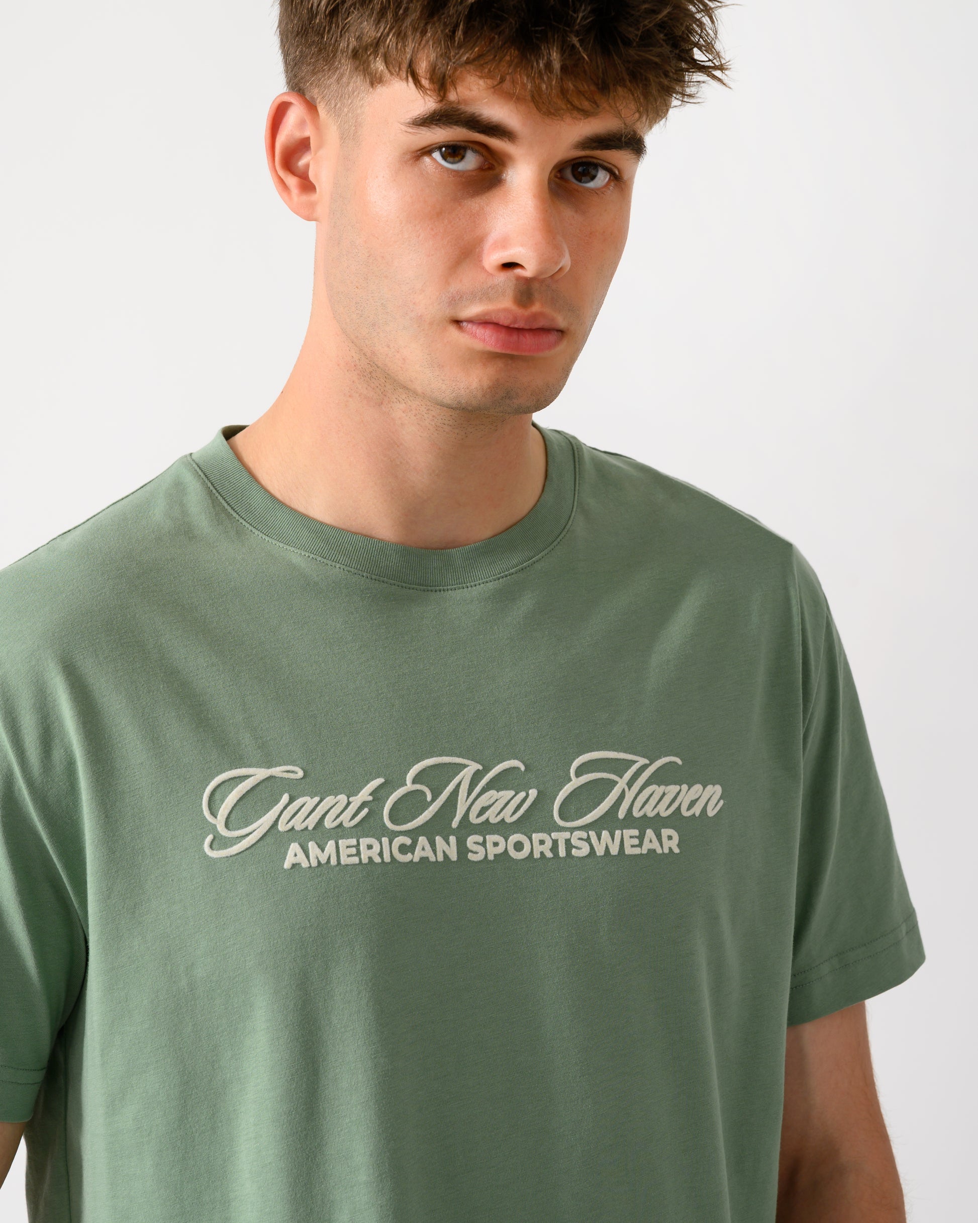 close up shot of a model wearing a GANT Mens Logo Graphic Short Sleeve T-Shirt in 308 Surplus Mint