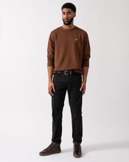 Wide shot of a model wearing a GANT Mens Regular Fit Shield Logo Crew Neck Sweatshirt in Mahogany Brown