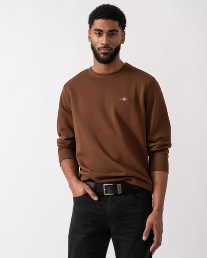 Model wearing a GANT Mens Regular Fit Shield Logo Crew Neck Sweatshirt in Mahogany Brown