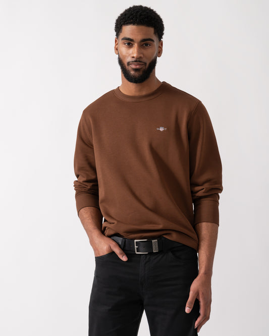 Model wearing a GANT Mens Regular Fit Shield Logo Crew Neck Sweatshirt in Mahogany Brown