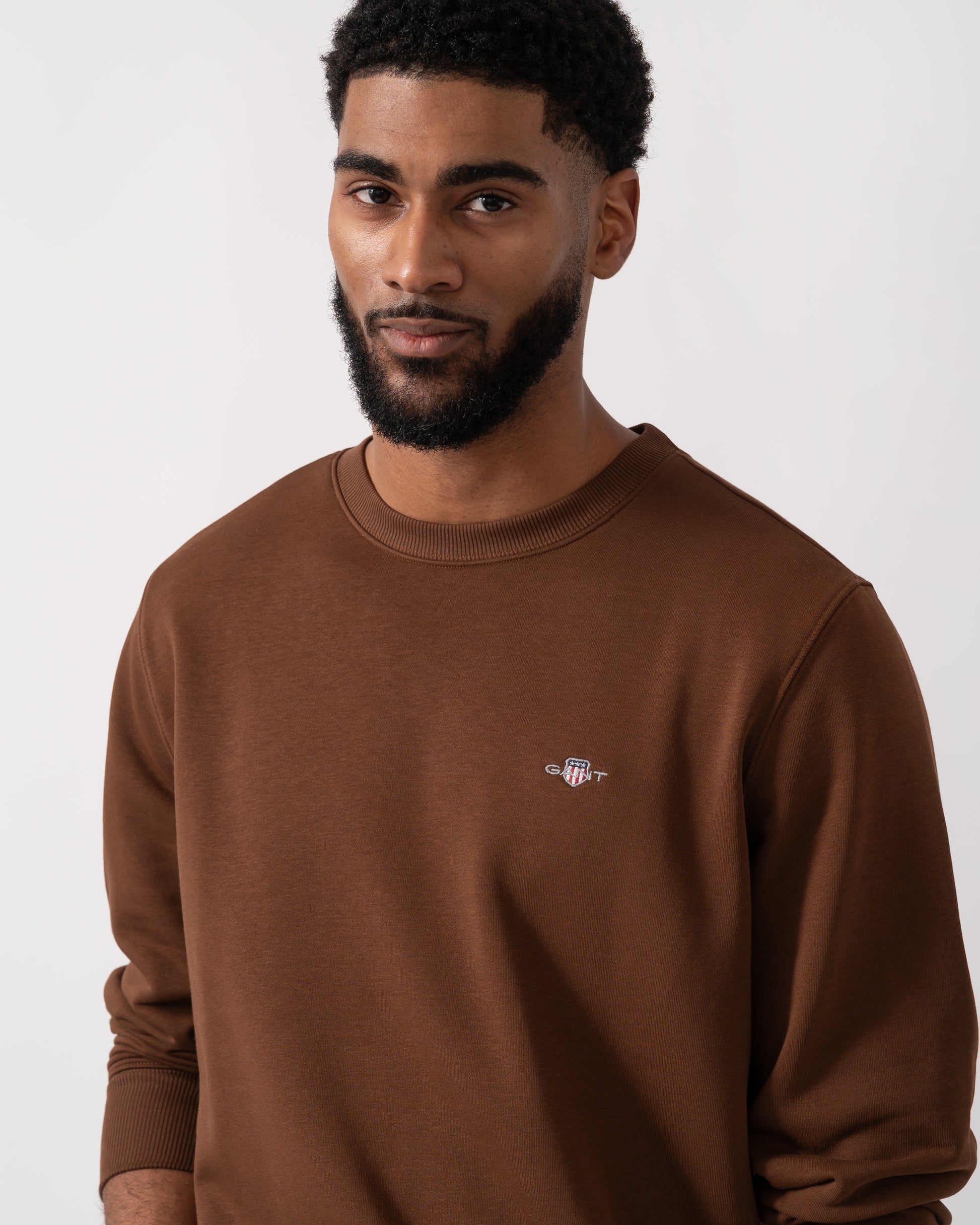 Close up shot of a model wearing a GANT Mens Regular Fit Shield Logo Crew Neck Sweatshirt in Mahogany Brown