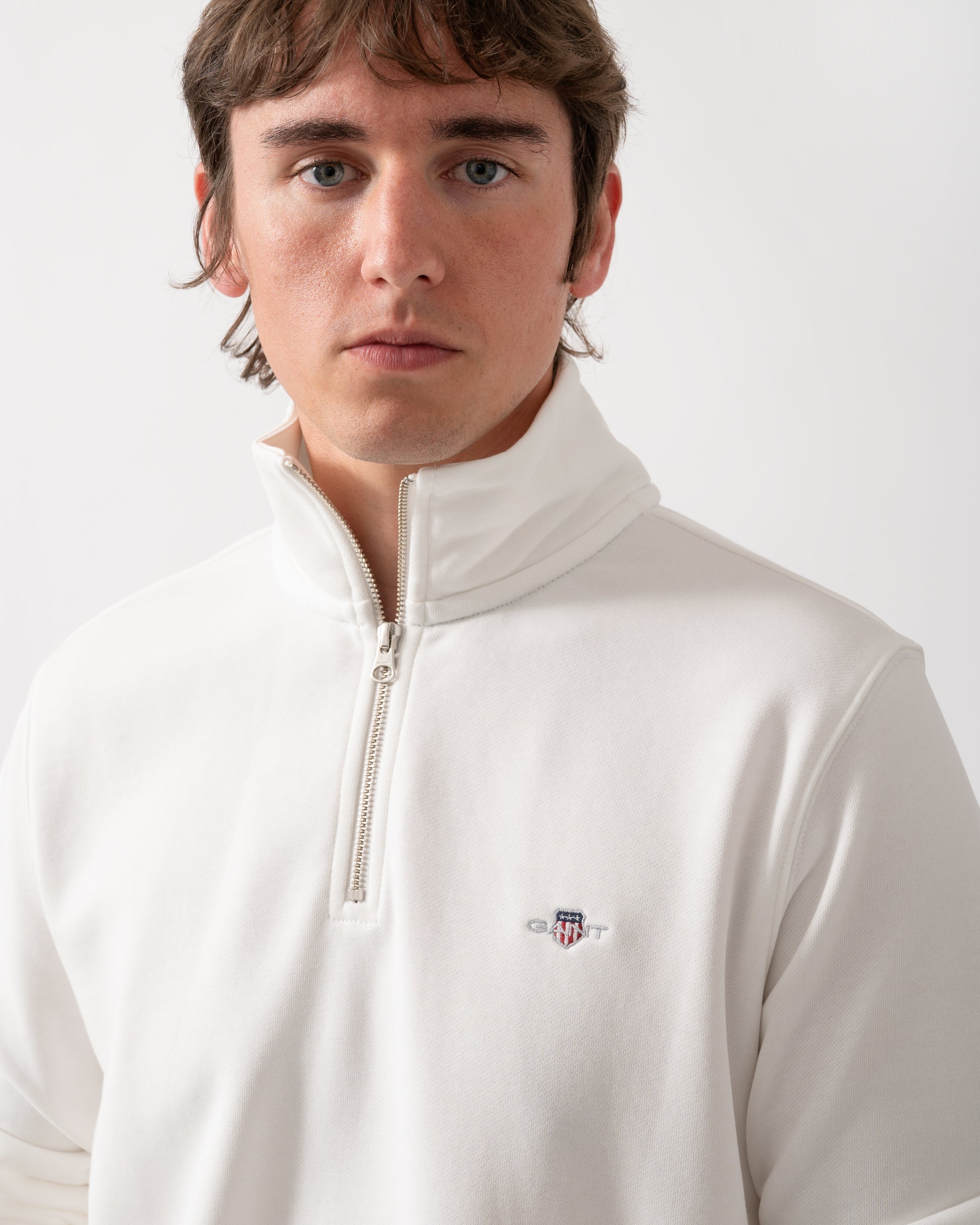 close up shot of a model wearing a GANT Mens Regular Fit Shield Logo Half Zip Sweatshirt in 113 Eggshell