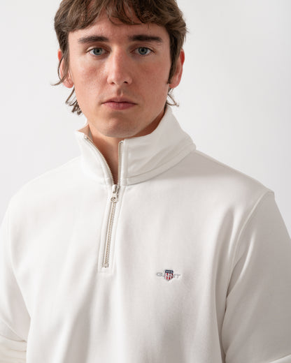close up shot of a model wearing a GANT Mens Regular Fit Shield Logo Half Zip Sweatshirt in 113 Eggshell