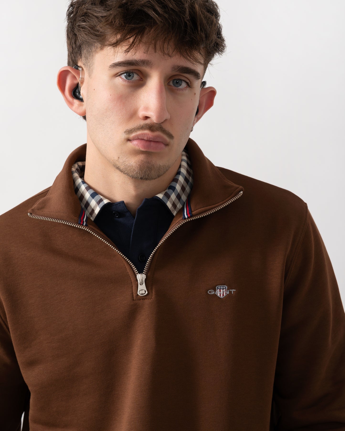close up shot of a model wearing a GANT Mens Regular Fit Shield Logo Half Zip Sweatshirt in 229 Mahogany Brown