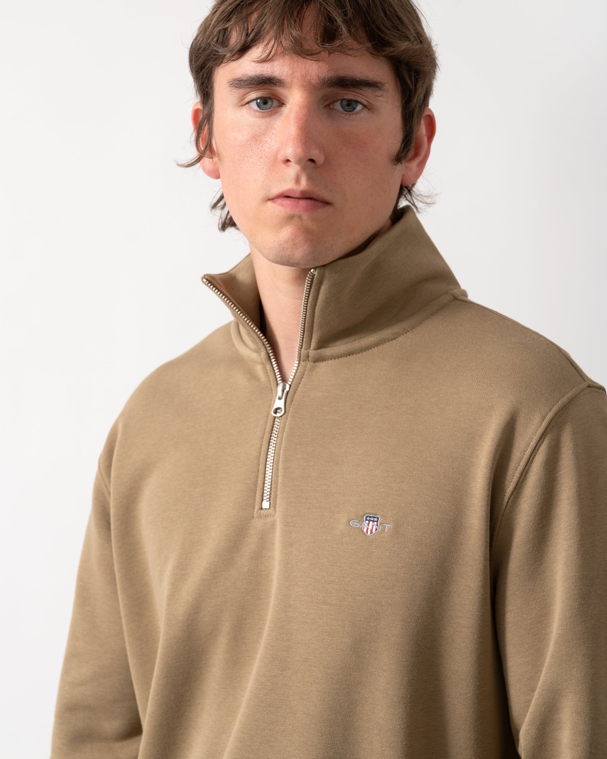 close up shot of a model wearing a GANT Mens Regular Fit Shield Logo Half Zip Sweatshirt in 264 Light Taupe