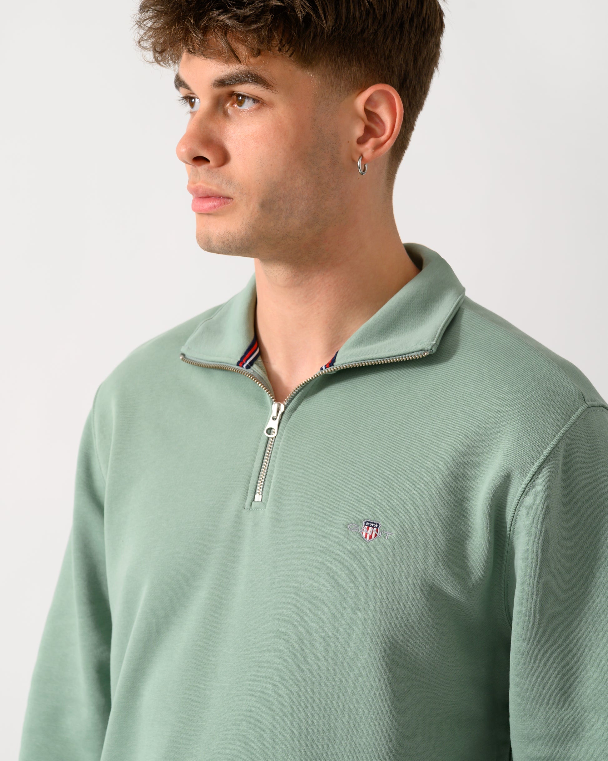 close up shot of a model wearing a GANT Mens Regular Fit Shield Logo Half Zip Sweatshirt in 308 Surplus Mint