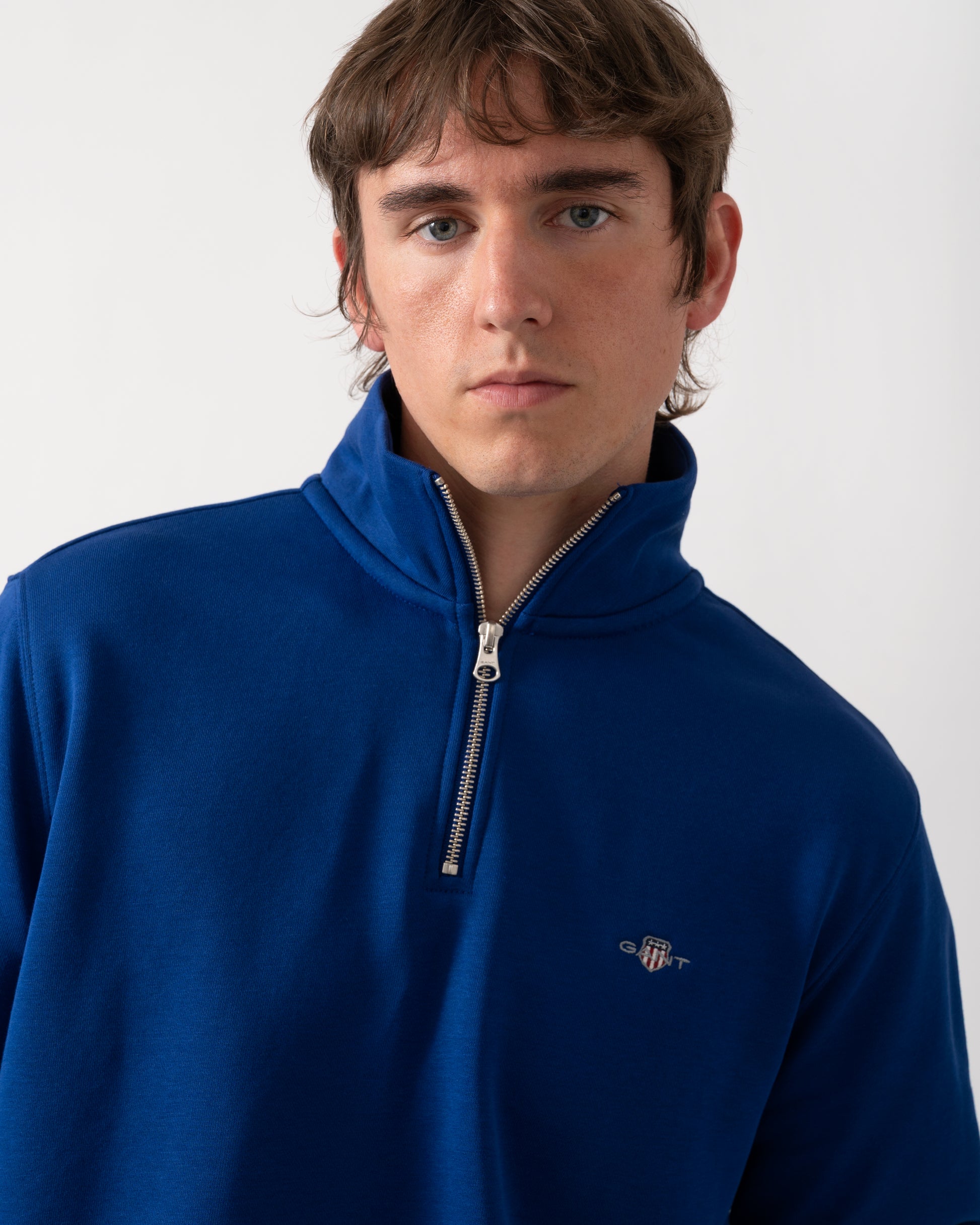 close up of model wearing a GANT Mens Regular Fit Shield Logo Half Zip Sweatshirt in 435 Crisp Blue