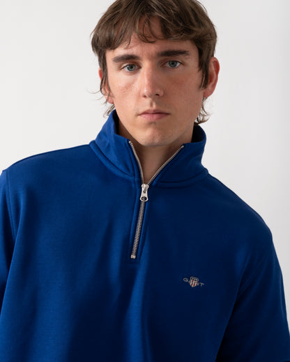 close up of model wearing a GANT Mens Regular Fit Shield Logo Half Zip Sweatshirt in 435 Crisp Blue