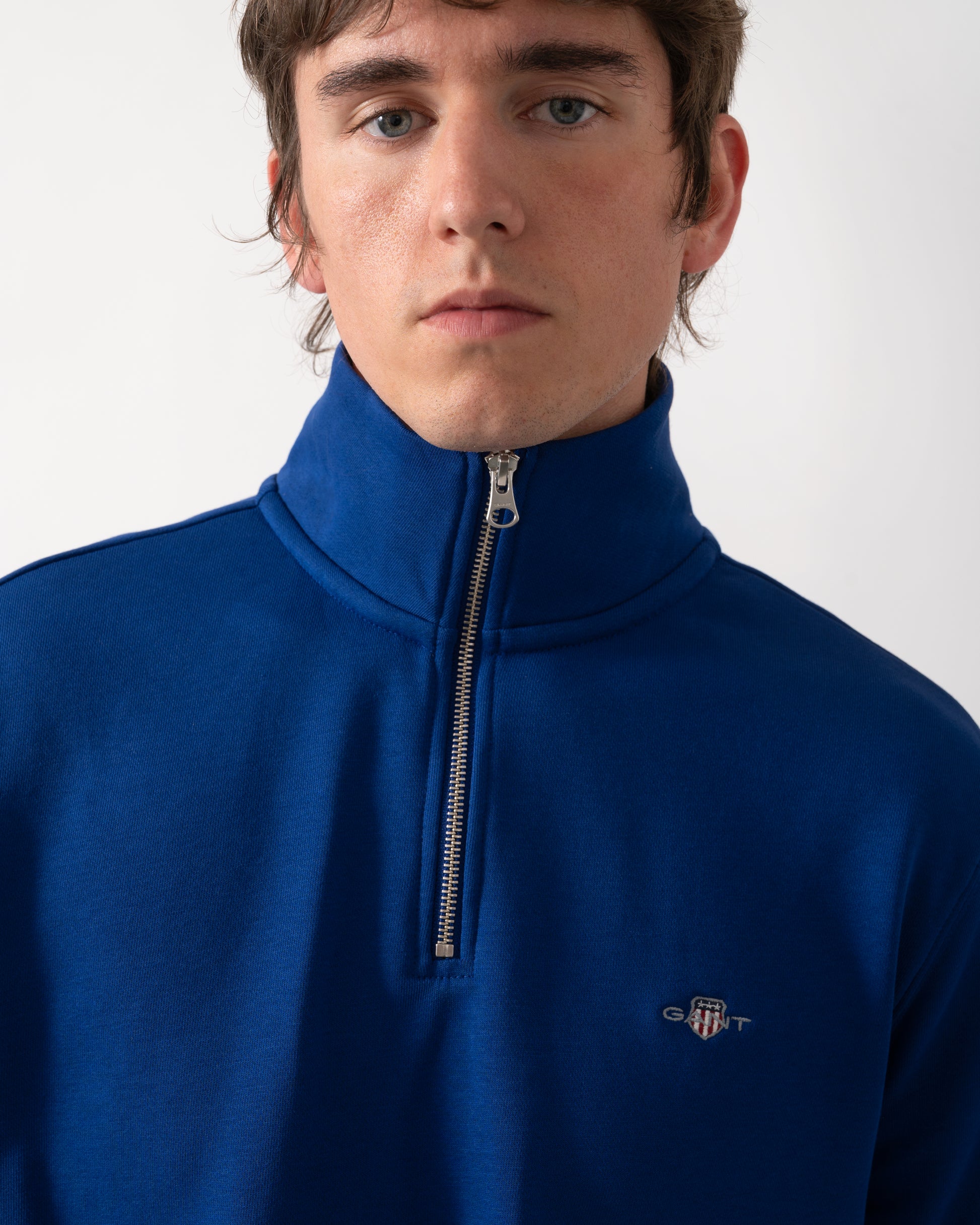detail of model wearing a GANT Mens Regular Fit Shield Logo Half Zip Sweatshirt in 435 Crisp Blue