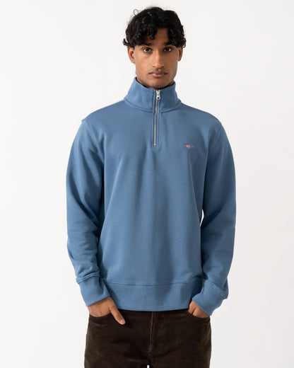 Studio photograph of a model wearing a GANT Mens Regular Fit Shield Logo Half Zip Sweatshirt in 476 Blue Horizon