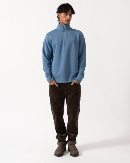 full length Studio photograph of a model wearing a GANT Mens Regular Fit Shield Logo Half Zip Sweatshirt in 476 Blue Horizon