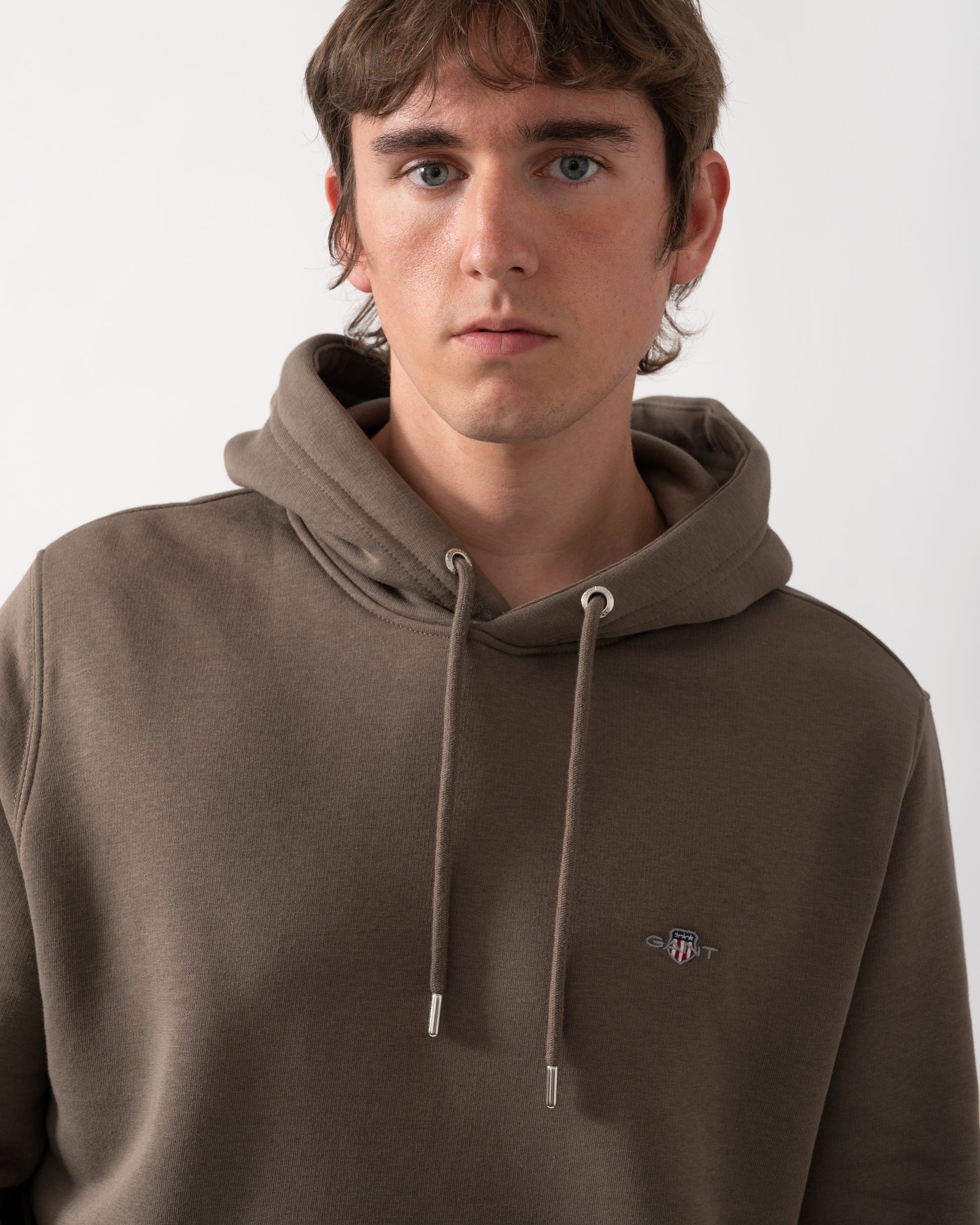 close up model wearing a GANT Mens Regular Fit Shield Logo Pullover Hoodie in 260 Faded Taupe