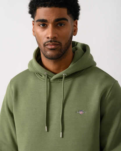 close up shot of a model wearing a GANT Mens Regular Fit Shield Logo Pullover Hoodie in 379 Dry Herb Green